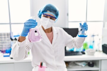 Young latin woman wearing scientist uniform holding test tubes at laboratory