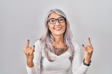 Middle age woman with grey hair standing over white background shouting with crazy expression doing rock symbol with hands up. music star. heavy music concept.