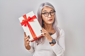 Middle age woman with grey hair holding gift winking looking at the camera with sexy expression,...