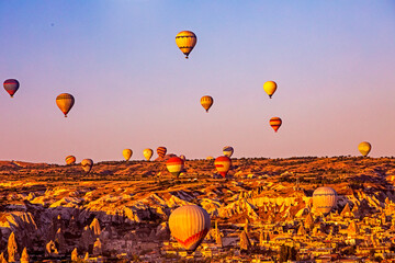 many balloons flying in the morning blue sky over the goreme valley with bizarre limestone shapes,...