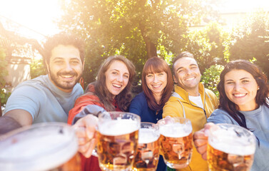Group of  friends toasting beer glasses outdoors in the farm - Group of students having fun at birthday party in the garden restaurant