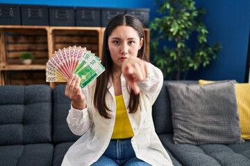 Young latin woman holding norwegian money pointing with finger to the camera and to you, confident...