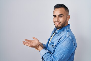 Fototapeta premium Young hispanic man standing over isolated background pointing aside with hands open palms showing copy space, presenting advertisement smiling excited happy
