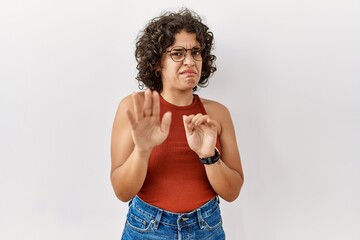 Young hispanic woman wearing glasses standing over isolated background disgusted expression,...