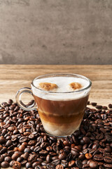  One cup of coffee with milk and coffee beans on wooden surface