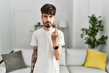 Hispanic man with beard at the living room at home showing middle finger, impolite and rude fuck off expression