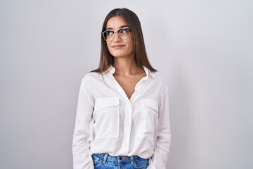 Young brunette woman wearing glasses smiling looking to the side and staring away thinking.