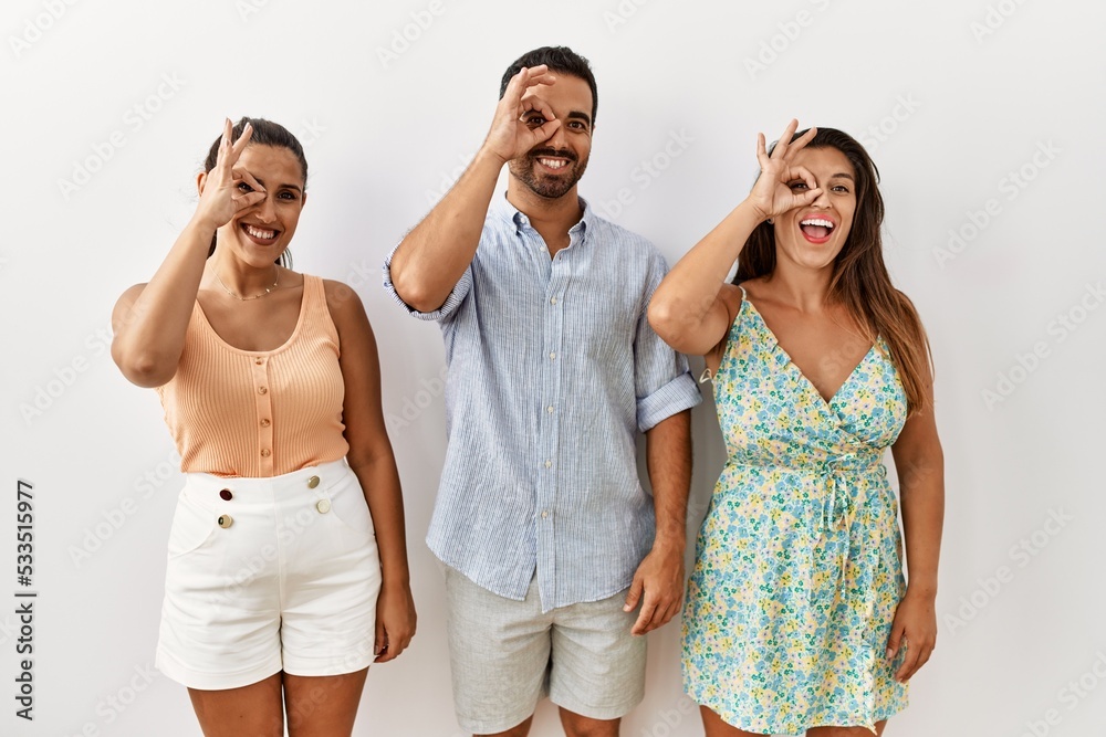 Poster Group of young hispanic people standing over isolated background smiling happy doing ok sign with hand on eye looking through fingers