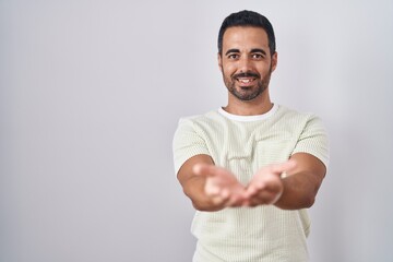 Fototapeta premium Hispanic man with beard standing over isolated background smiling with hands palms together receiving or giving gesture. hold and protection