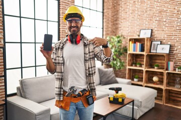 Young hispanic man with beard working at home renovation holding smartphone pointing finger to one self smiling happy and proud