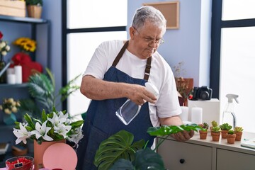 Middle age grey-haired man florist using diffuser working at florist