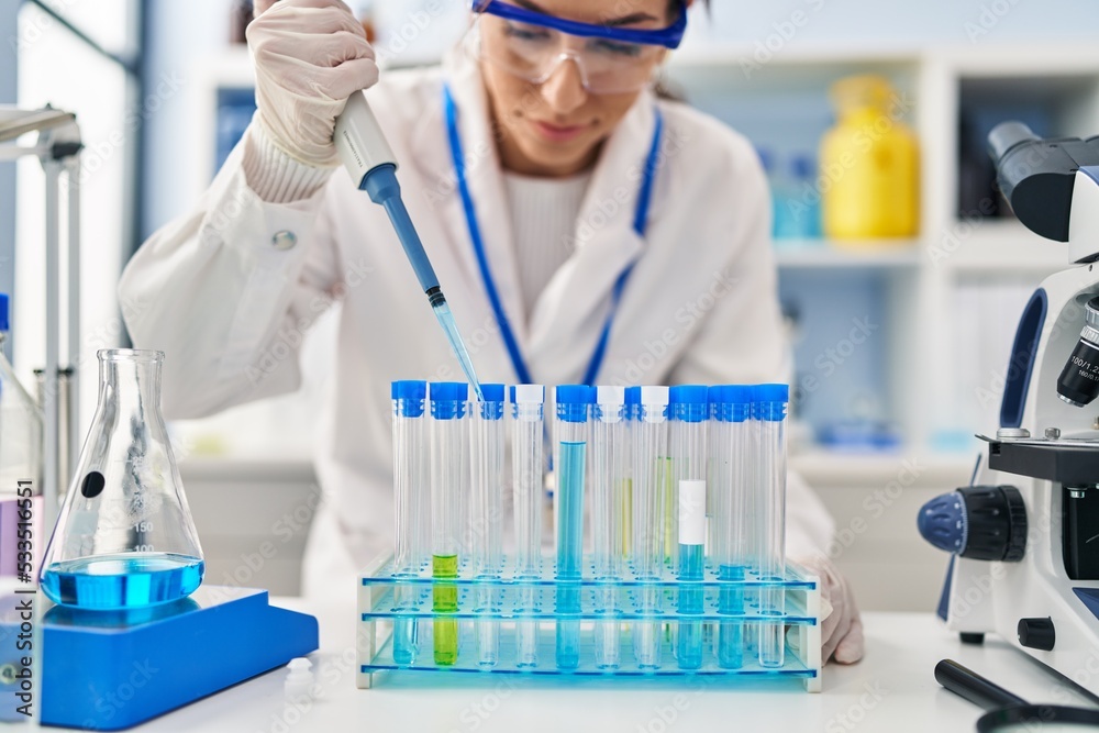 Canvas Prints Young hispanic woman wearing scientist uniform using pipette at laboratory