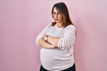 Obraz premium Pregnant woman standing over pink background skeptic and nervous, disapproving expression on face with crossed arms. negative person.