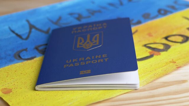 Hand Thrown a Biometric Passport of Ukraine on Table with of Ukrainian Flag. Child drawing of yellow, blue Ukrainian flag with inscription Ukraine cries tears of blood lies on table. War, migrants.