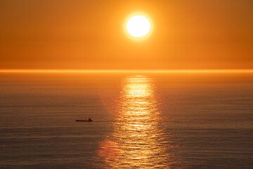 Wonderful landscapes in Norway. Nord-Norge. Beautiful scenery of a midnight sun sunset at Nordkapp (Cape North). Boat and globe on a cliff. Rippled sea and clear orange sky. Selective focus