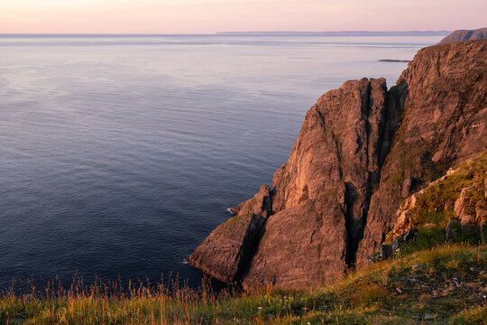Wonderful landscapes in Norway. Nord-Norge. Beautiful scenery of a midnight sun sunset at Nordkapp (Cape North). Boat and globe on a cliff. Rippled sea and clear orange sky. Selective focus