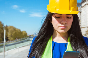 young latin woman engineer, reading a text message with instructions from her boss