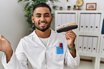 Young indian man holding teeth whitening palette celebrating achievement with happy smile and winner expression with raised hand