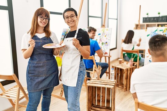 Two woman smiling happy drawing with group of people at art studio.