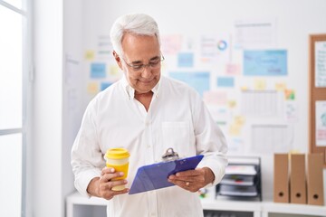 Middle age grey-haired man business worker reading document drinking coffee at office