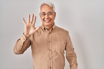 Hispanic senior man wearing glasses showing and pointing up with fingers number five while smiling confident and happy.