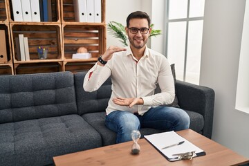 Young hispanic man with beard working at consultation office gesturing with hands showing big and large size sign, measure symbol. smiling looking at the camera. measuring concept.