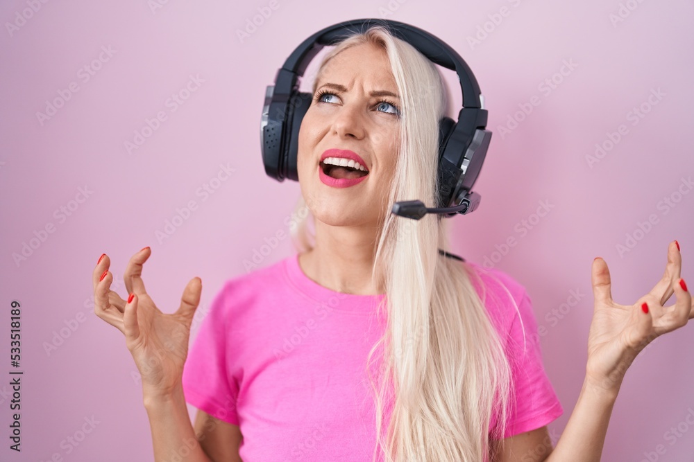 Wall mural caucasian woman listening to music using headphones crazy and mad shouting and yelling with aggressi