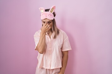 Blonde caucasian woman wearing sleep mask and pajama tired rubbing nose and eyes feeling fatigue and headache. stress and frustration concept.