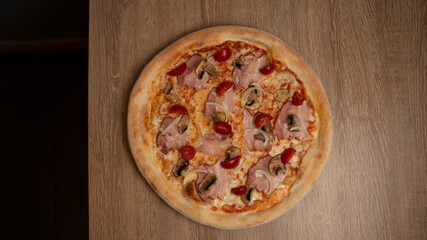 Italian pizza with cheese, ham, cherry tomatoes, onions and mushrooms on the table background