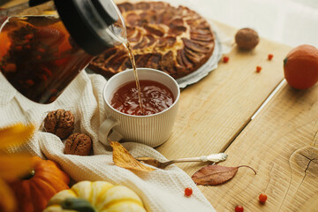 Pouring herbal tea in stylish cup on background of wooden table with freshly baked warm apple pie...