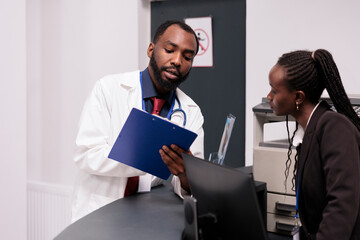 Naklejka na ściany i meble African american team working on checkup reports at hospital reception desk, analyzing patients appointments on papers. Doctor and receptionist using medical forms to help people with disease.