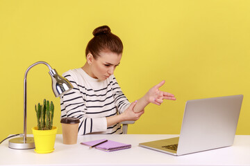 Aggressive woman manager sitting at workplace with laptop threatening and pointing finger gun to...