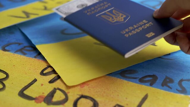 Hand Takes a Biometric Passport of Ukraine with Cash on a Background of Flag. Inscription in Ukrainian Ukraine Passport. Drawings of yellow, blue Ukrainian flag with the title stop war lie on table.