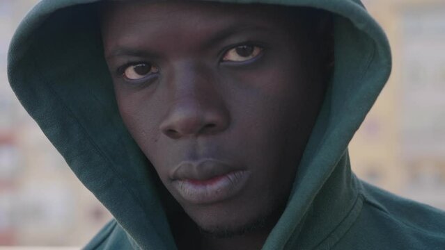 Close up on serious sad young hooded black african migrant staring at camera