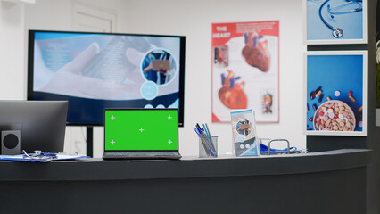 Empty reception desk with greenscreen on laptop display, hospital lobby counter. Computer with blank chroma key screen, isolated mockup template and copyspace background display.
