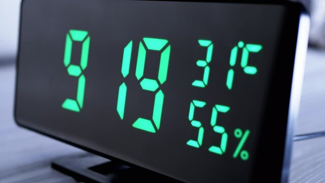 Digital Clock Showing Time on Green Display 9:19 AM, Temperature, Air Humidity. Modern mirror clock, alarm clock with a thermometer, hydrometer standing on a desk on white background. Time concept.