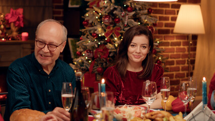 Beatiful wife at home enjoying Christmas dinner with loved ones while smiling heartily at camera. Festive happy people celebrating winter holiday with traditional home cooked food.