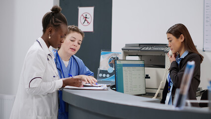 Medical assistant and doctor analyzing report papers at reception counter, working on checkup forms...