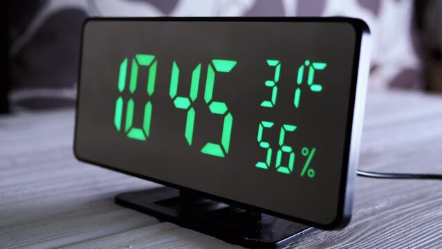 Digital Clock Showing Time on Green Display 10:45 AM, Temperature, Air Humidity. Modern mirror clock, alarm clock with a thermometer, hydrometer standing on a desk on white background. Time concept.
