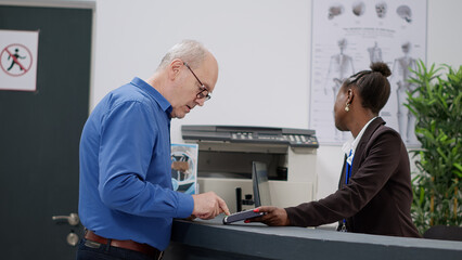 Senior patient paying checkup appointment and treatment at reception desk with credit card. Making...
