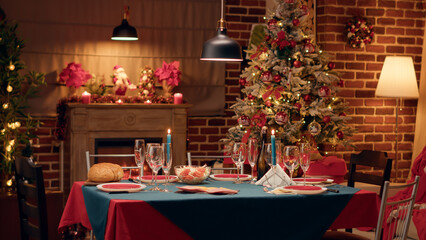 Empty interior of festive and ornate Christmas dinner table in living decorated with traditional garlands. Cozy and warm looking dining room with positive style with nobody in it. Tripod shot
