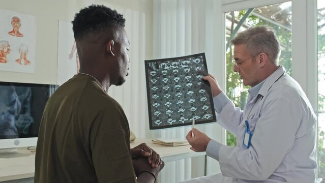 Medium shot of doctor discussing CT scan image with African American soldier during medical consultation in hospital