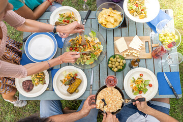 Multicultural family sitting at wooden table having dinner. They have plates full of food and glasses with drinks.
