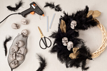 DIY halloween wreath background. Process of making wreath with glue gun, black feathers, skulls and...
