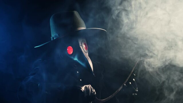 Plague doctor with sharp sickle isolated on blue smoke background. Creepy raven mask, halloween, historical terrible protection costume, mystical fantasy. Epidemic, death concept