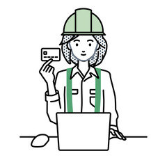 Obraz na płótnie Canvas デスクで座ってPCを使いながらクレジットカードを手に持っている工事現場の女性