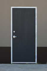 An image of a single industrial exterior door painted dark grey in color. 