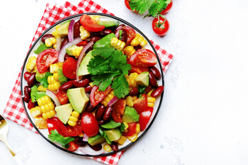Mexican spicy salad with corn, red beans, avocado, jalapeno, tomatoes, onion and cilantro. White stone table background, top view