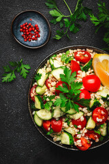 Bulgur tabbouleh salad with fresh tomatoes, cucumbers, parsley and lemon dressing. Traditional Middle Eastern and Arabic dish. Black stone kitchen table background, top view