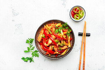 Asian cuisine, stir fry with chicken, red paprika pepper and zucchini bowl. White kitchen table background, top view, copy space